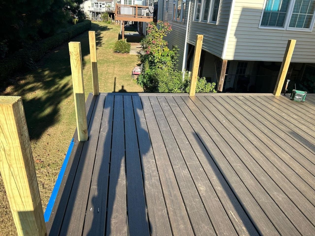 Dark composite decking with new railing posts overlooking a backyard