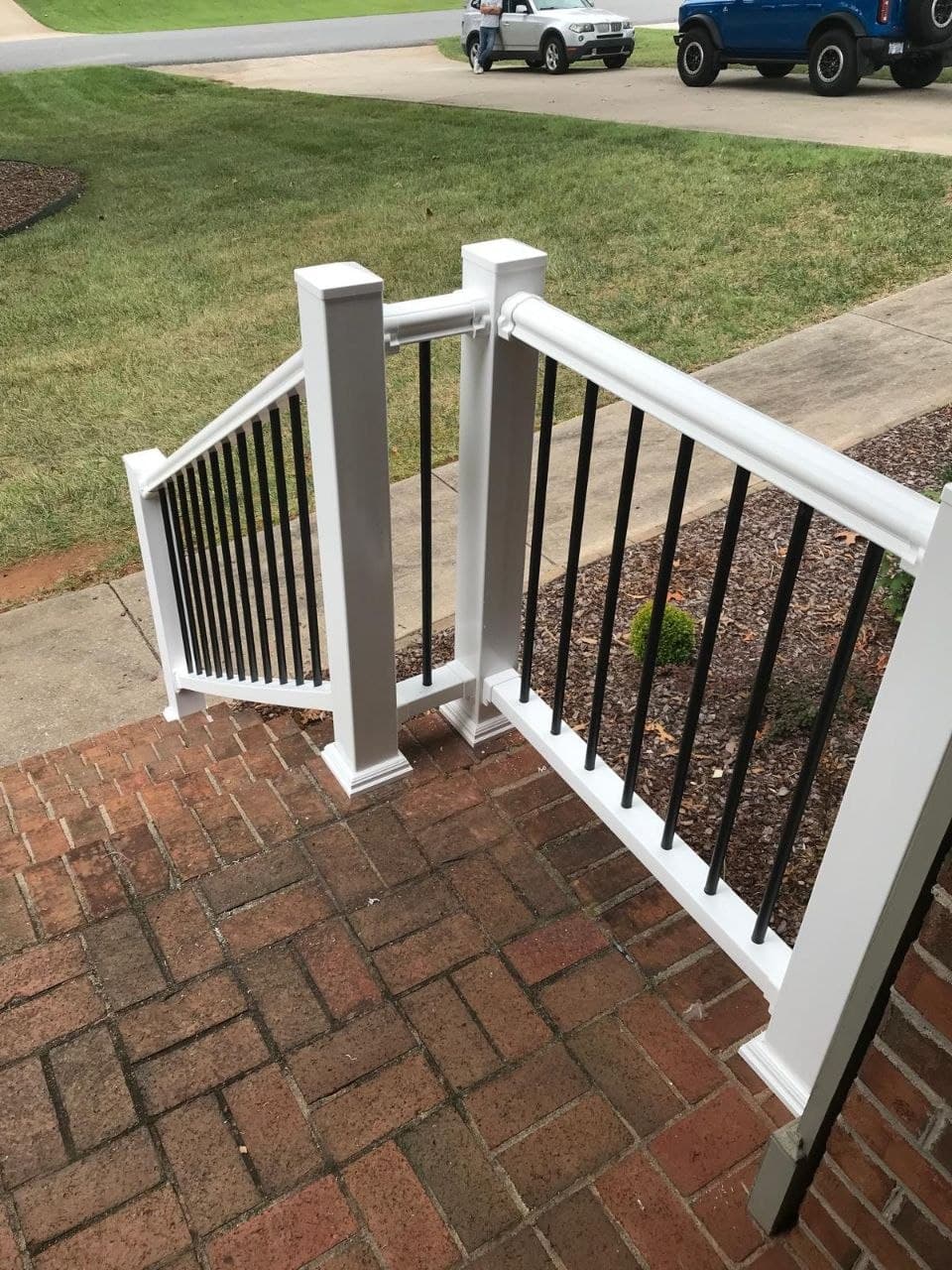 White railing with black balusters installed at brick front steps